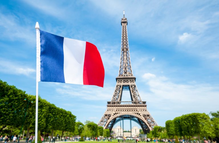 French flag flying in bright blue sky above the Eiffel Tower in